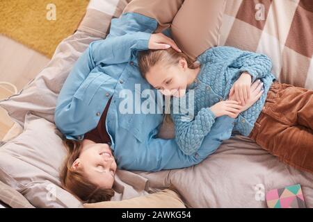 Top view ritratto di madre felice abbracciando cute ragazza e sorridendo l'uno l'altro mentre sdraiato a letto a casa, copia spazio Foto Stock