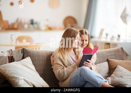 Ritratto caldo-tonato di ragazza carina che dà la carta fatta a mano per la mamma in Mothers giorno, copia spazio Foto Stock