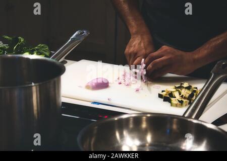 Primo piano delle mani dell'uomo che tagliano le cipolle su un tagliere in una cucina professionale Foto Stock