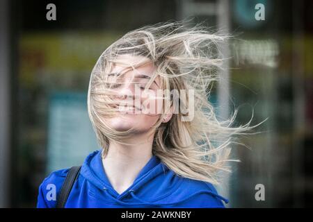 Una ragazza donna che ha una brutta giornata di capelli come i suoi capelli che soffiano nel tempo del vento causando i grovigli come la forza gale venti spazzare attraverso le strade Foto Stock