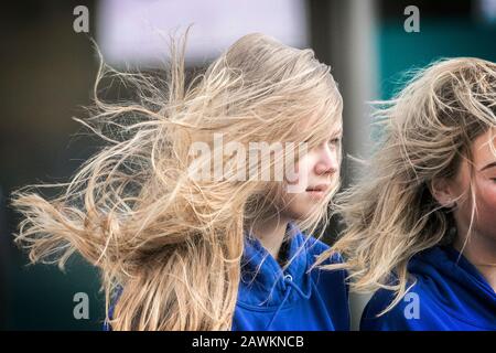 Una ragazza donna che ha una brutta giornata di capelli come i suoi capelli che soffiano nel tempo del vento causando i grovigli come la forza gale venti spazzare attraverso le strade Foto Stock