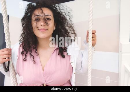Bella giovane donna con capelli ricci su un'altalena che guarda la macchina fotografica Foto Stock