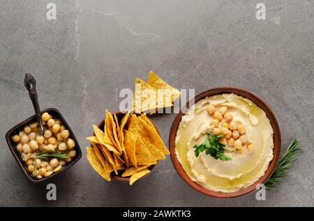 Piatto Lay Hummus in piatto di argilla condito con ceci e foglie di coriandolo verde su tavolo di pietra servito con tortilla patatine Foto Stock