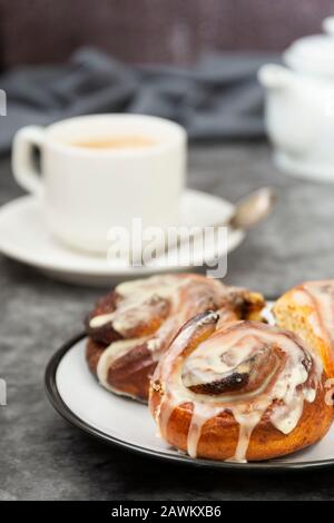 Cannella, bun danese o cinabro su sfondo scuro con tazza da caffè. Dolce pasticceria fatta in casa. Foto Stock