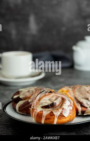 Cannella, bun danese o cinabro su sfondo scuro con tazza da caffè. Dolce pasticceria fatta in casa. Foto Stock