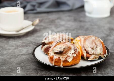 Cannella, bun danese o cinabro su sfondo scuro con tazza da caffè. Dolce pasticceria fatta in casa. Foto Stock