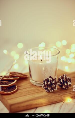 White candela che brucia con decorazioni e ghirlanda di luci in bokeh di fondo su un tavolo di legno. Casa accogliente e concetto di hygge Foto Stock