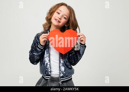 Ragazza che tiene un grande cuore rosso 3d fatto di carta per San Valentino su uno sfondo chiaro. Foto Stock