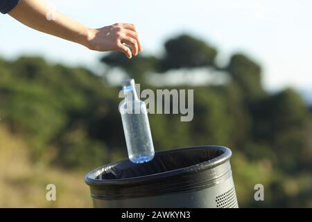 Primo piano di una mano di donna che getta una bottiglia di plastica in bidone in un parco o in un ambiente verde Foto Stock