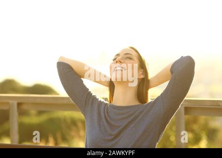 Donna felice che riposa seduta su una panchina al tramonto con le braccia sulla testa Foto Stock