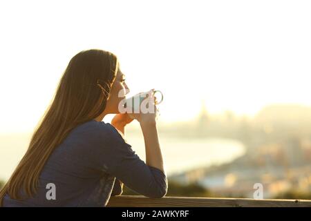 La ragazza felice beve caffè contemplando le viste da un balcone al tramonto