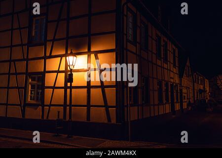 Una stretta strada lungo il medievale tipiche case a graticcio nella città vecchia di Quedlinburg illuminati dalla luce calda delle lampade di sera Foto Stock