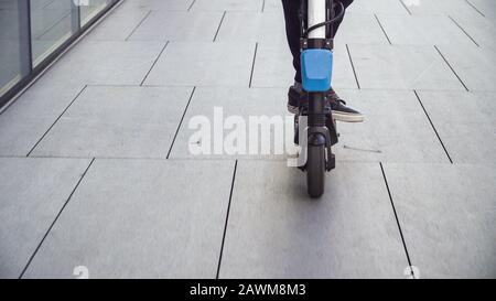 Vestirsi di giovani studenti di lavoro casual uomo a cavallo scooter elettrico su un marciapiede in una città d'affari Foto Stock