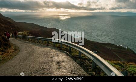 Persone che camminano verso il Mull of Kintyre faro con vista verso l'Irlanda del Nord e Rathlin isola in condizioni meteorologiche drammatiche in inverno, Scot Foto Stock