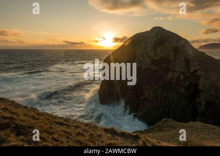 Roaring Cove al Castello di Dunaverty e Dunaverty Rock con vedute dietro il Mull of Kintyre al tramonto, in Scozia Foto Stock