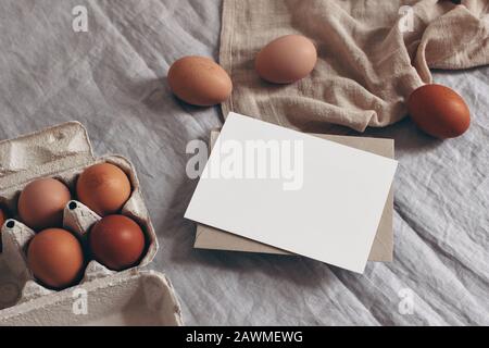 Primavera mockup scena. Biglietto di auguri vuoto, invito al tavolo. Pasqua, design fattoria. Foto in borsa dallo stile naturale femminile. Uova di pollo e asciugamano da tè Foto Stock