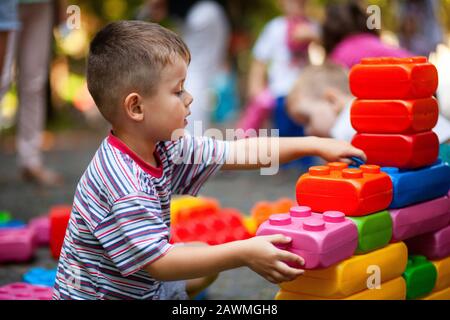 Carino ragazzo giocando con il giocattolo edili blocchi colorati. Il capretto con faccia felice giocando con mattoni di plastica. Plastica giocattolo di grandi dimensioni. Foto Stock