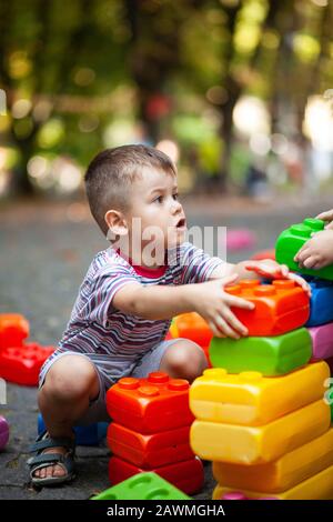 Carino ragazzo giocando con il giocattolo edili blocchi colorati. Il capretto con faccia felice giocando con mattoni di plastica. Plastica giocattolo di grandi dimensioni. Foto Stock