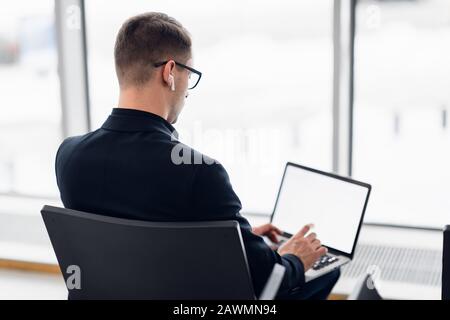 Giovane uomo d'affari seduto sul computer all'aeroporto in attesa del volo. Vista dal retro Foto Stock