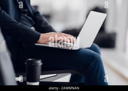Giovane uomo d'affari seduto sul computer all'aeroporto in attesa del volo. Vista ravvicinata dal lato Foto Stock