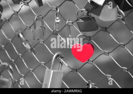 Lucchetto nella forma rossa del cuore sulla recinzione di un ponte. Sfondo monocromatico. Simbolo dell'amore per sempre. Foto Stock