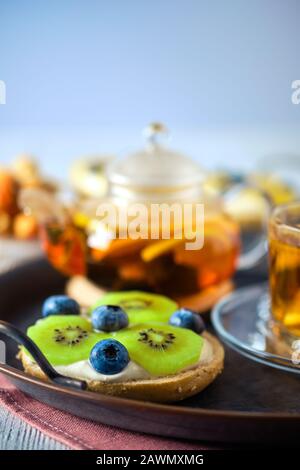 foto di fuoco selettivo di formaggio cottage su un fresco bun con kiwi e mirtillo e tè sullo sfondo Foto Stock