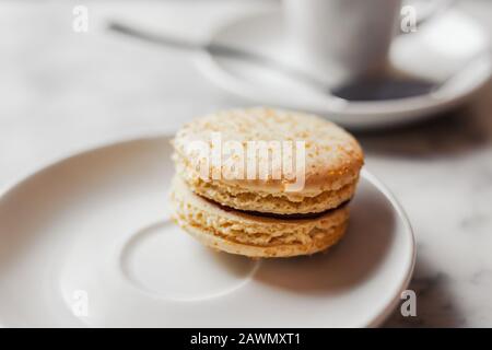 Primo piano foto di macaron con caramello salato su un piattino bianco con una tazza di caffè sfocata sullo sfondo Foto Stock