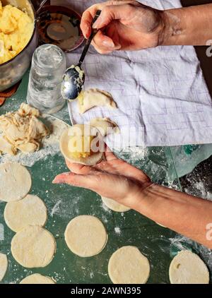 Donna che usa un cucchiaio con le mani scolpisce gnocchi con patate in cucina nazionale Ucraina, primo piano. Foto Stock