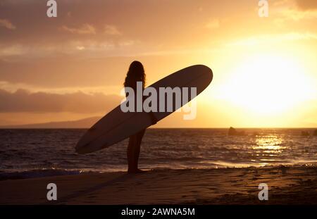 Surfista femminile guarda il tramonto a White Rock, Maui, Hawaii. Foto Stock