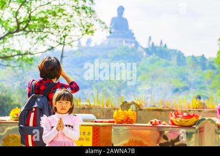 Hong Kong, Cina - 11 dicembre 2016: Donna con bambina che prega il Grande Buddha nel monastero di po Lin sull'isola di Lantau. Religione popolare Cinese Foto Stock