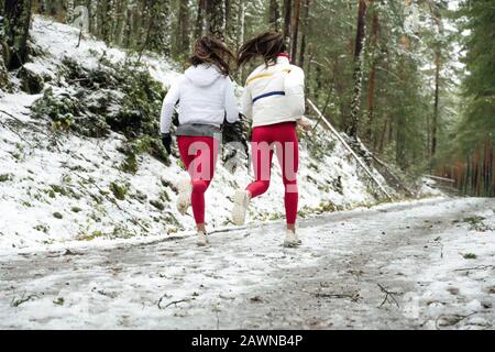 Gemelle atletiche femminili che corrono in una foresta coperta di neve al mattino presto Foto Stock