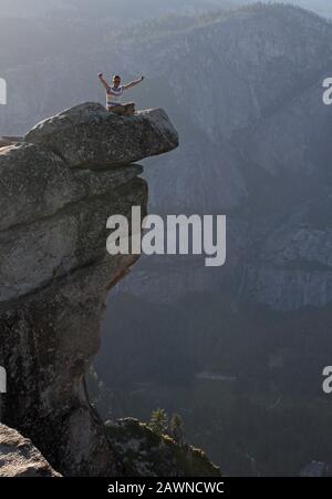 Scatto verticale di un uomo seduto su una scogliera dentro Il Parco Nazionale di Yosemite negli Stati Uniti Foto Stock
