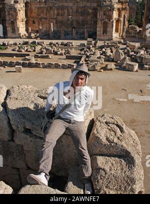 Colpo verticale di un ragazzo in un cappello seduto sopra una pietra vicino a rovine storiche Foto Stock