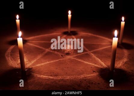 Simbolo di pentagramma bianco su terreno in cemento. Illuminato con candele. Sfondo scuro. Occultismo spaventoso e mistico Foto Stock