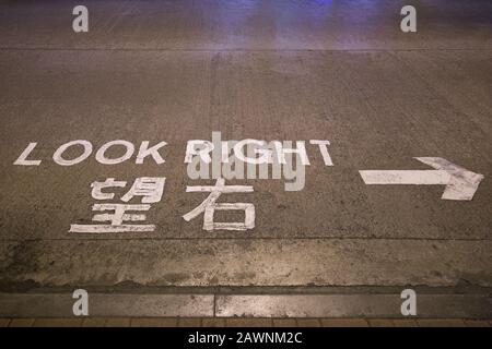 Freccia e 'guardare a destra' attenzione o segno scritto in inglese e cinese su una strada a Hong Kong, Cina. Foto Stock