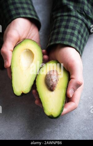 Mani maschili che tengono metà avocado. Alimentazione sana, stile di vita sano, concetto di dieta vegetariana Foto Stock