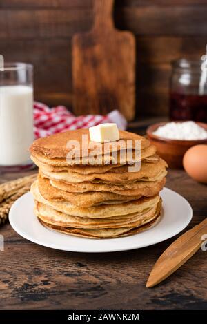 Pila di crespi sottili, blini con burro su piastra bianca. Maslenitsa, Concetto Di Martedì Di Shrove. Orientamento verticale, stile rustico Foto Stock