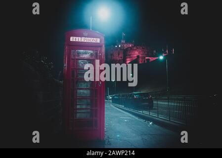 Edimburgo, Scozia, 13 dicembre 2018: il vecchio Britannico rosso phone booth di fianco alla strada di notte con castello in background. Foto Stock