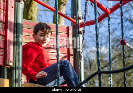 Un ragazzo felice di giocare su una cornice di arrampicata in un parco giochi per bambini. Foto Stock
