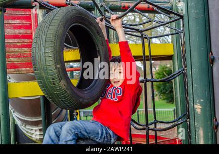 Un ragazzo felice di giocare su una cornice di arrampicata in un parco giochi per bambini. Foto Stock
