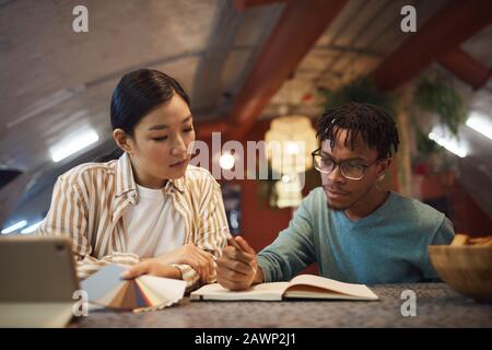 Ritratto di due giovani etnici che lavorano insieme al progetto mentre siedono al tavolo in ufficio Foto Stock