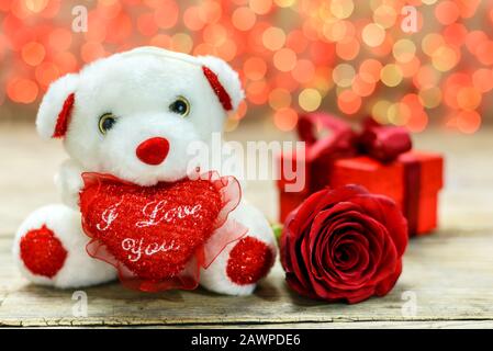 Concetto di giorno di San Valentino. Orsacchiotto bianco, scatola regalo e rosa rossa su un vecchio tavolo in legno di fronte a uno sfondo luminoso sfocato con spazio copia per t. Foto Stock