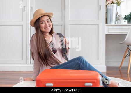 Giovane viaggiatore asiatico donna preparare stoffa e roba in valigia arancione per vacanza a casa.zaino in spalla concetto di viaggio Foto Stock