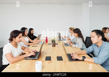 Giovani sviluppatori di software che lavorano su laptop a grande tavolo da ufficio in legno Foto Stock