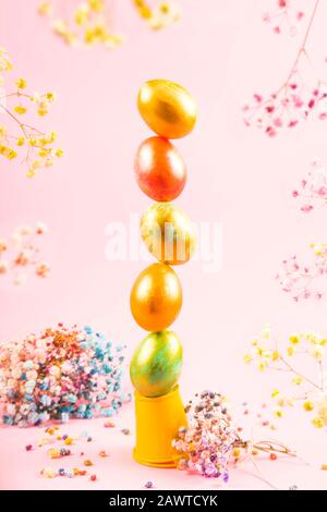 Le uova di Pasqua dipinte sono disposte in una torre verticale e si equilibrano su uno sfondo rosa tra i fiori. Concetto creativo di pasqua. Foto Stock