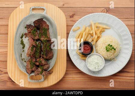 Bistecca con riso e patatine fritte su 2 piatti sopra la vista in tavolo di legno Foto Stock