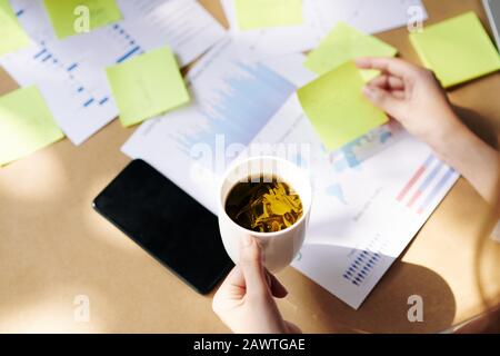 Analista finanziario bere tè alle erbe quando lavora con i rapporti e ponderare su nuove idee per lo sviluppo di affari Foto Stock