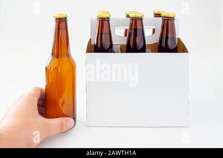 Una persona che tiene una birra con un pacchetto di sei bottiglie di birra marrone isolato su sfondo bianco Foto Stock