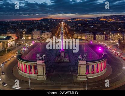 Budapest, Ungheria - veduta aerea del drone della famosa Piazza degli Eroi (Hosok tere) illuminata di notte in un unico colore viola e rosa con un tramonto colorato Foto Stock