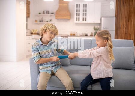 I bambini litigano, prendendo il tablet l'uno dall'altro Foto Stock